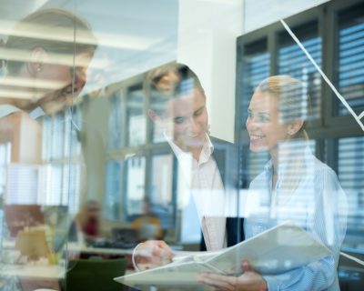 Smiling business team behind glass wall in office looking at folder